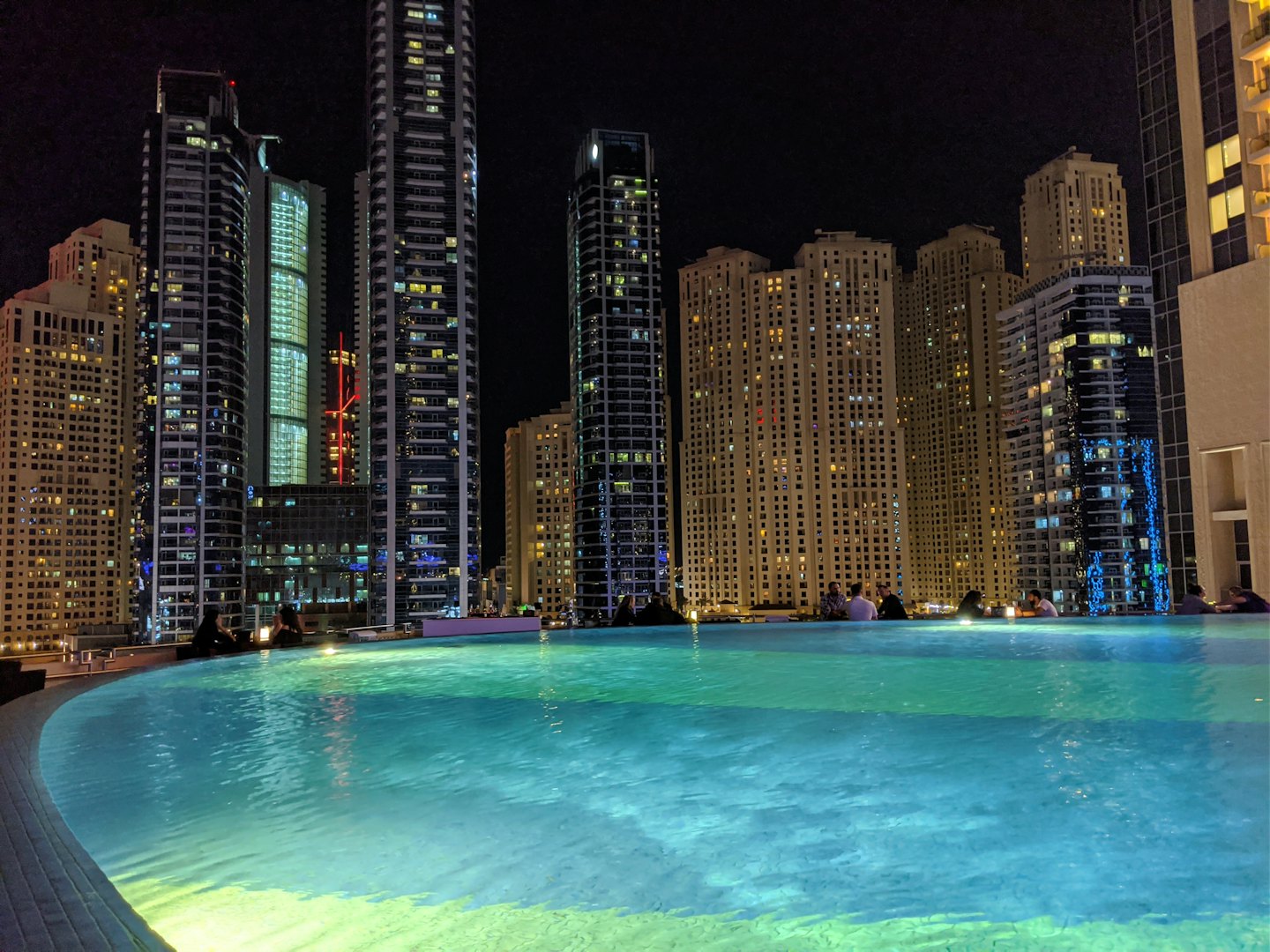Gente relajándose en una piscina infinita con vistas al horizonte urbano.